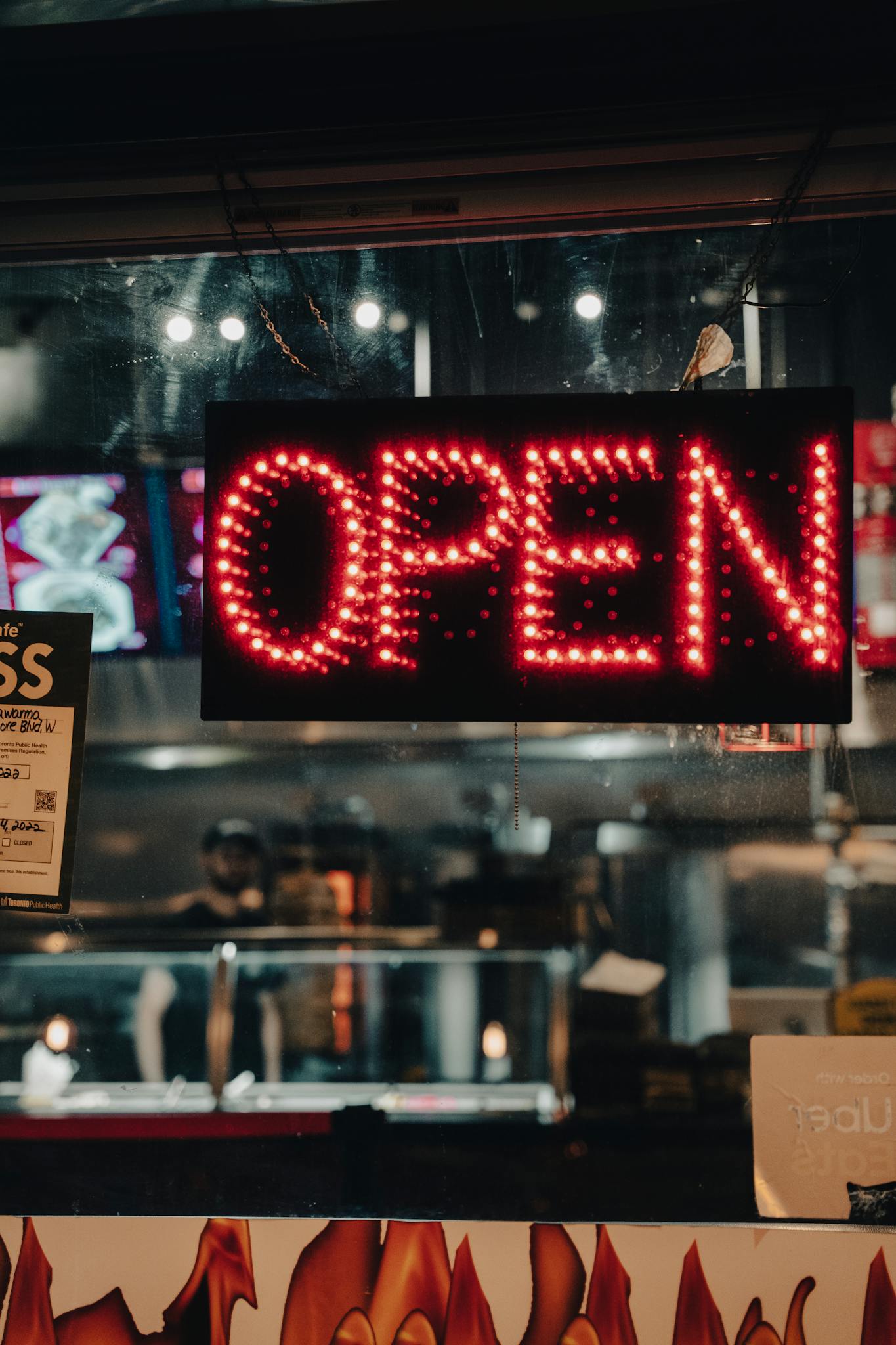 Close-up of a glowing red neon 'OPEN' sign in a dimly lit storefront window.