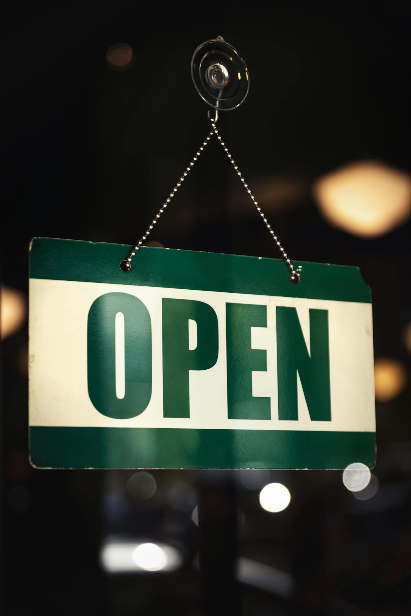 Close-up of a green 'Open' sign hanging in a shop window with bokeh background.